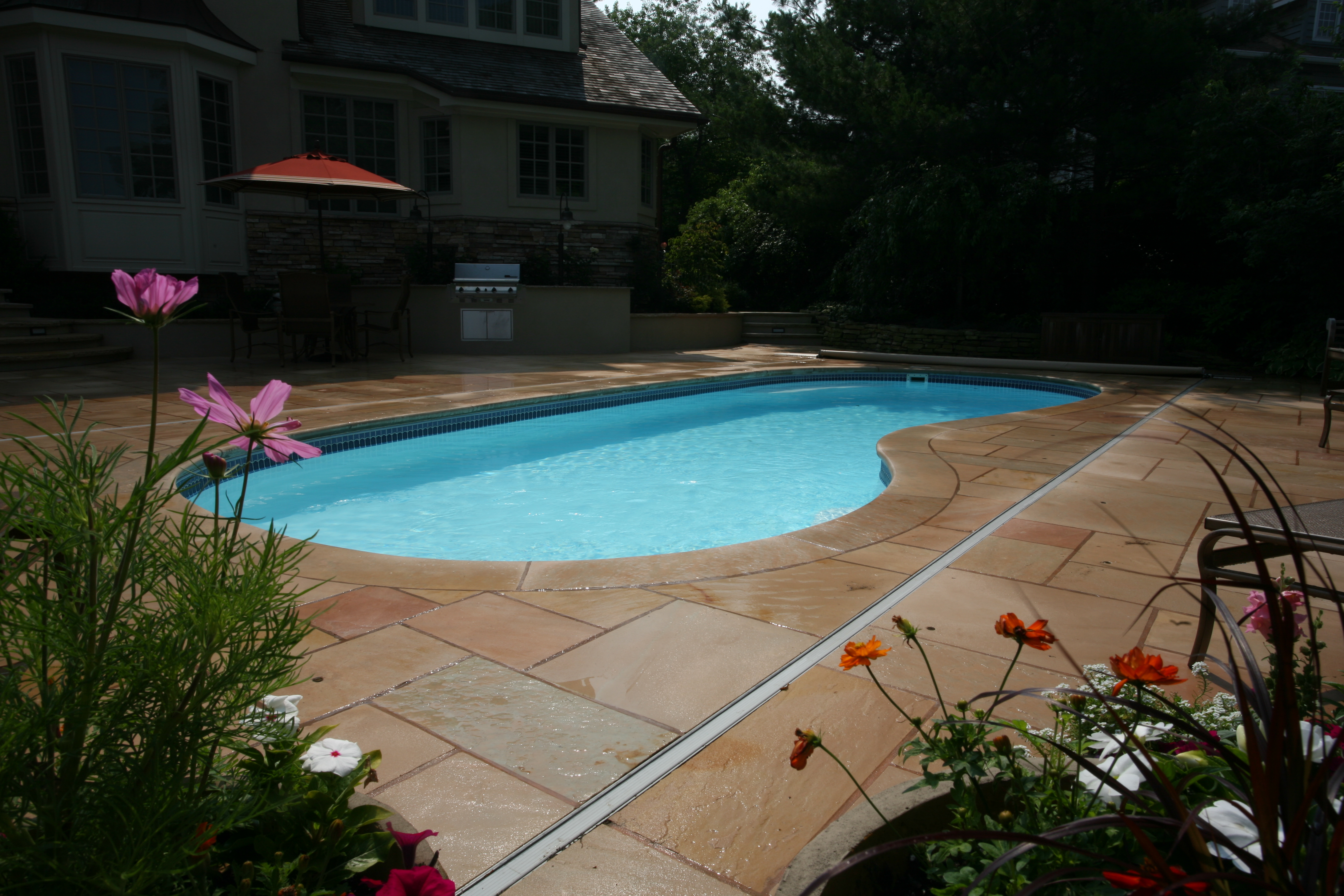 A serene backyard oasis featuring a beautifully installed inground pool, perfect for warm summer days and relaxation. The natural surroundings and classic aesthetic create a tranquil atmosphere ideal for unwinding.