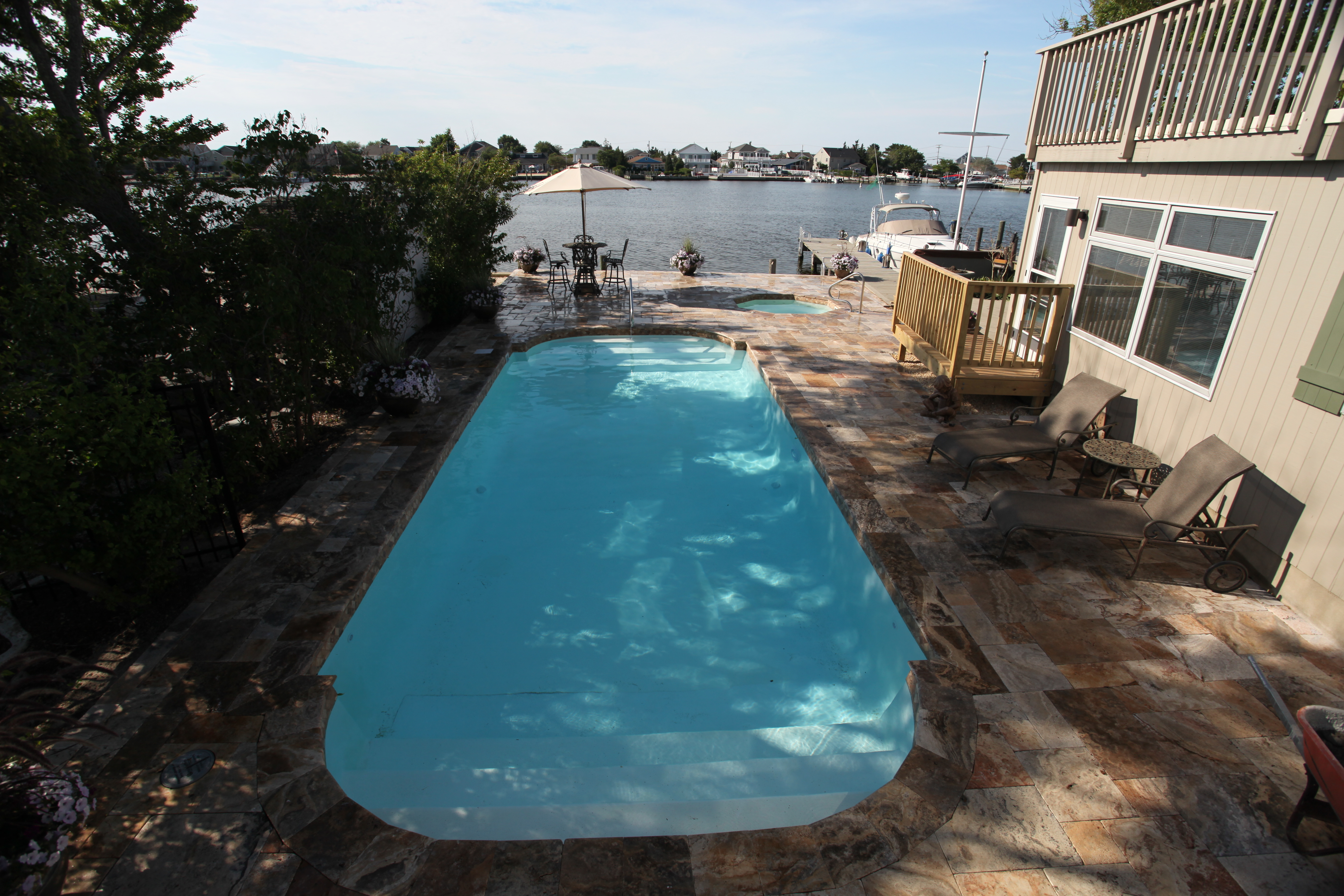 Experience serene luxury with this sun-kissed backyard fiberglass pool, framed by a stone patio and vibrant foliage.