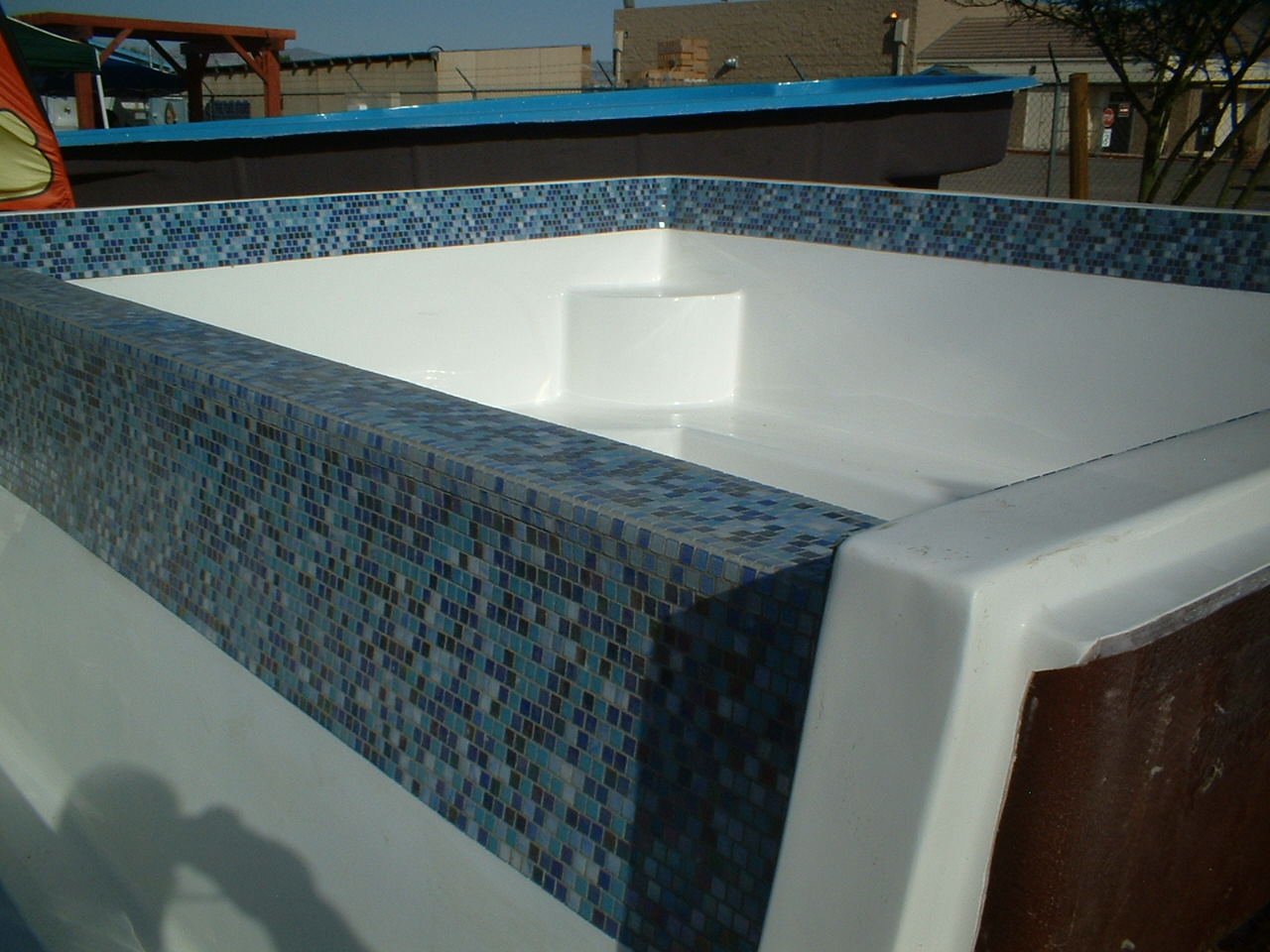Sun-lit showroom showcase of a sleek white fiberglass pool framed by a blue mosaic tile trim.