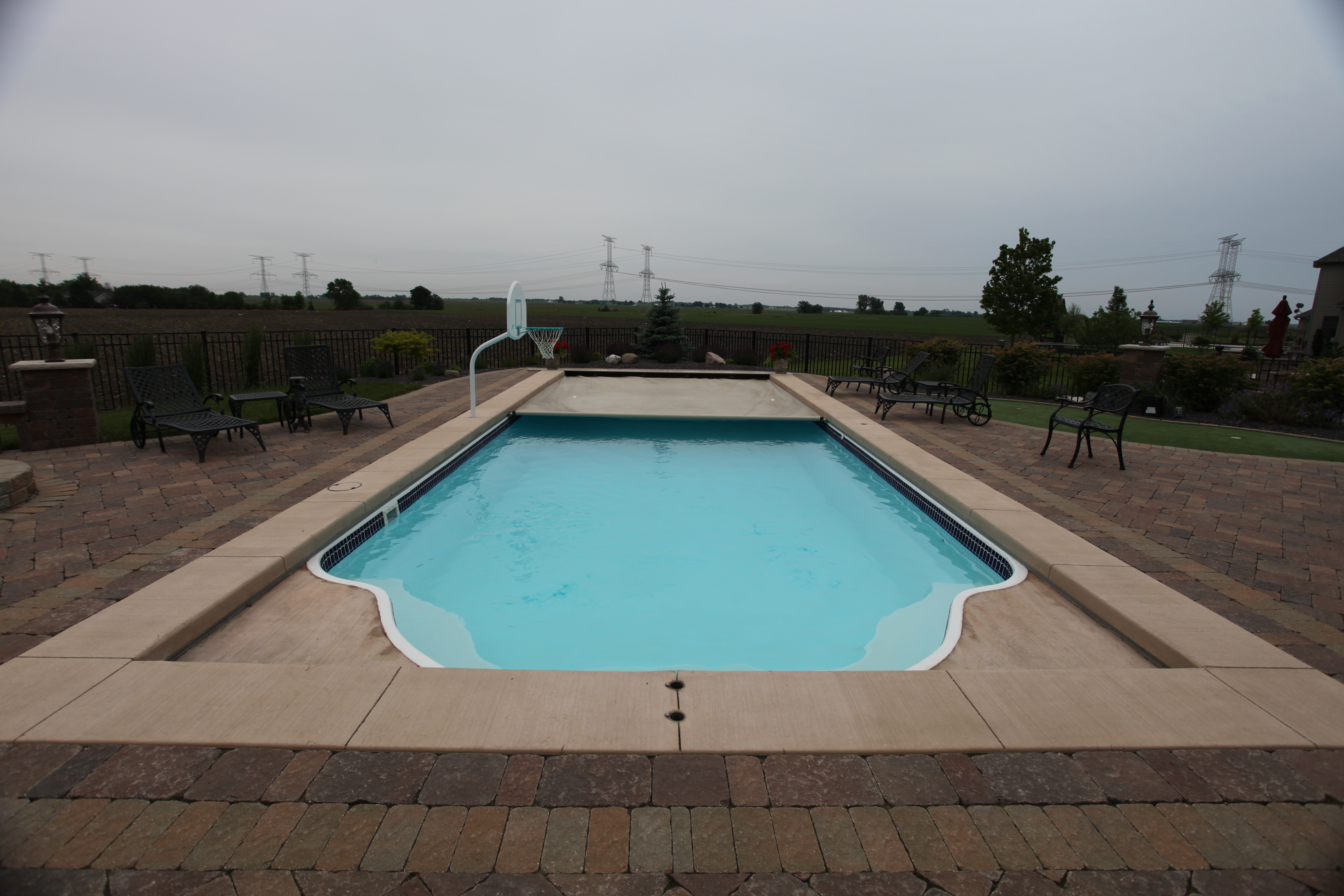 Enjoy a serene summer oasis with our expertly crafted fiberglass pool, nestled in a stylish backyard surrounded by a cozy brick patio and lounge chairs.