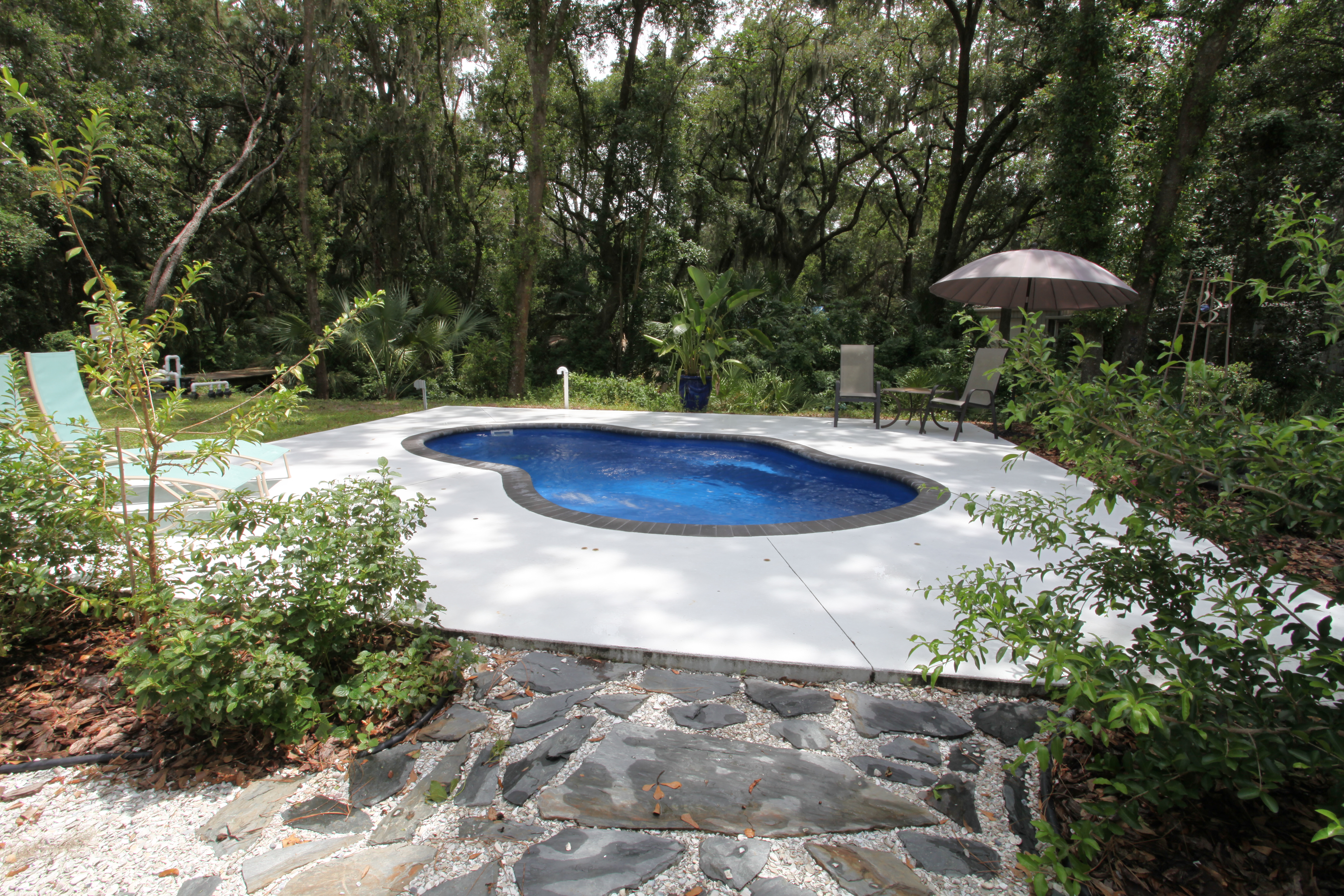 Escape to this serene backyard oasis featuring a stunning kidney-shaped fiberglass pool, surrounded by lush greenery and meticulously maintained landscaping.
