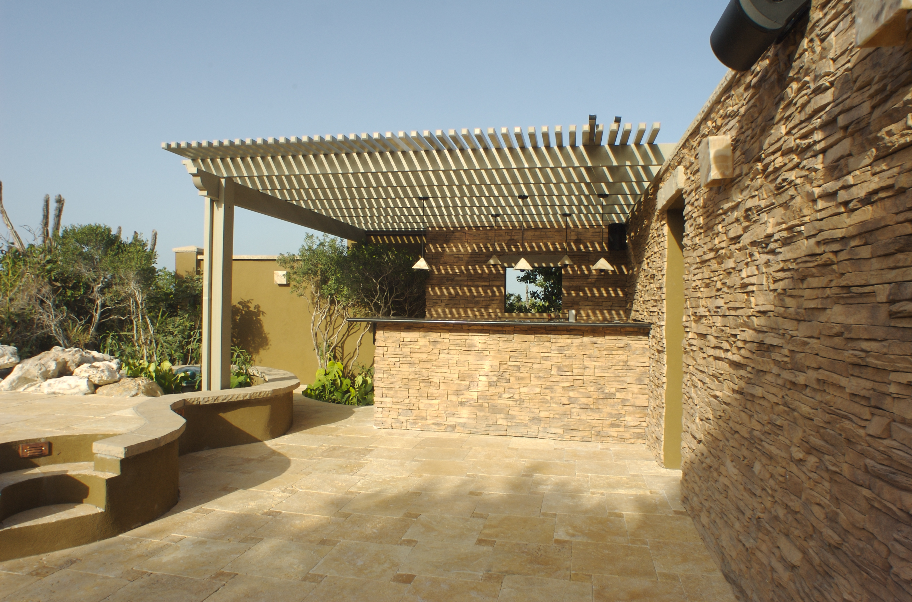 Enjoy the serene tropical patio featuring a stone wall, terracotta roof, wooden pergola, and outdoor kitchen—perfect for warm summer evenings.