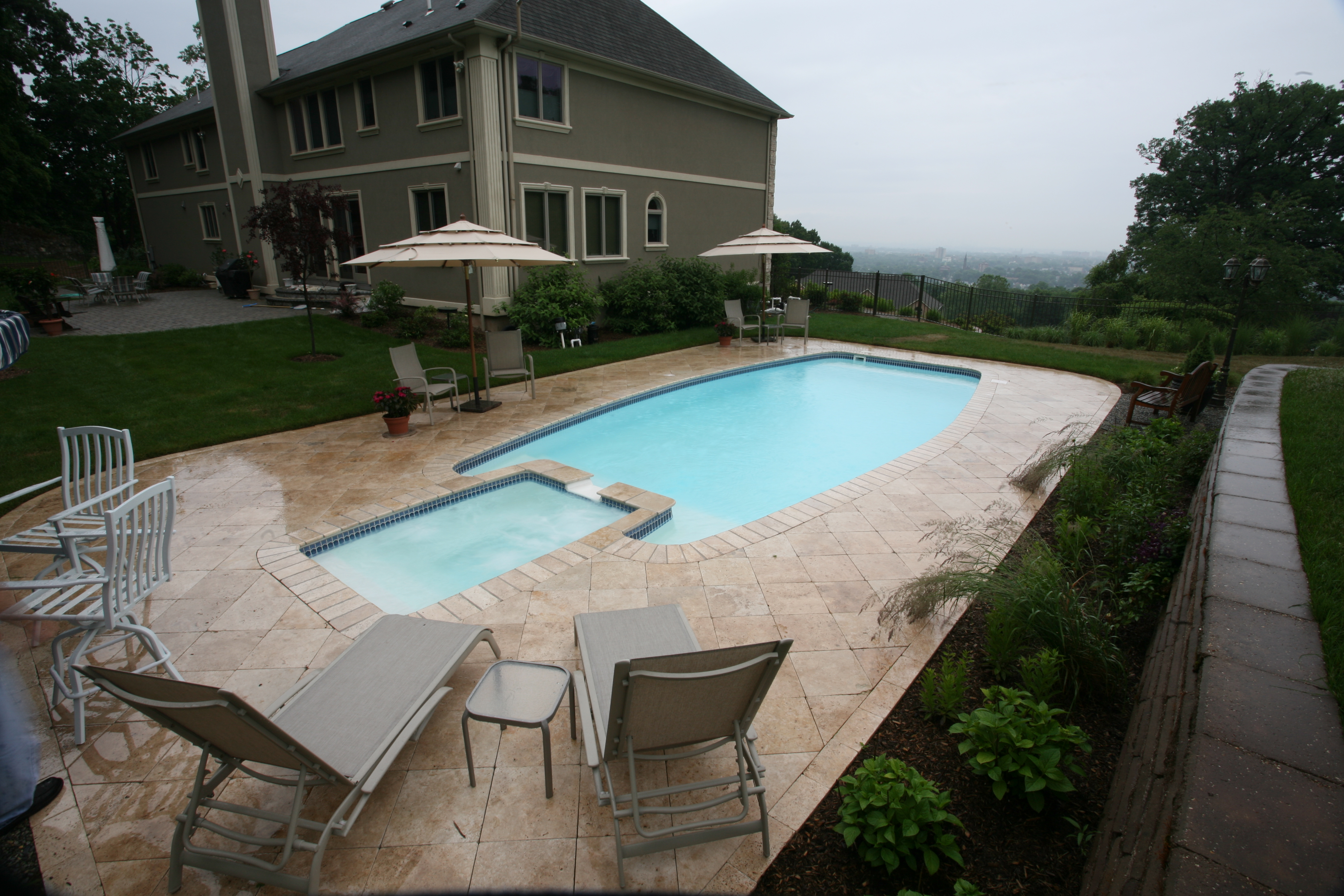 Enjoy the tranquility of a pristine fiberglass inground pool surrounded by a classic stone patio and shaded umbrellas—your personal backyard oasis.