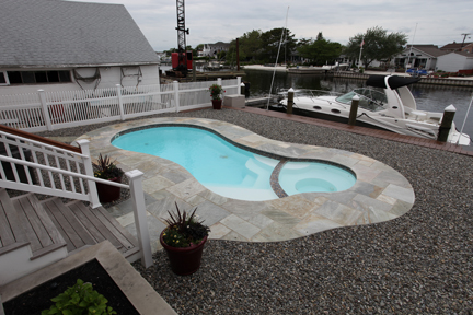 Escape to tranquility with this serene fiberglass pool nestled in a waterfront haven, surrounded by lush greenery and a blend of natural and man-made elements.