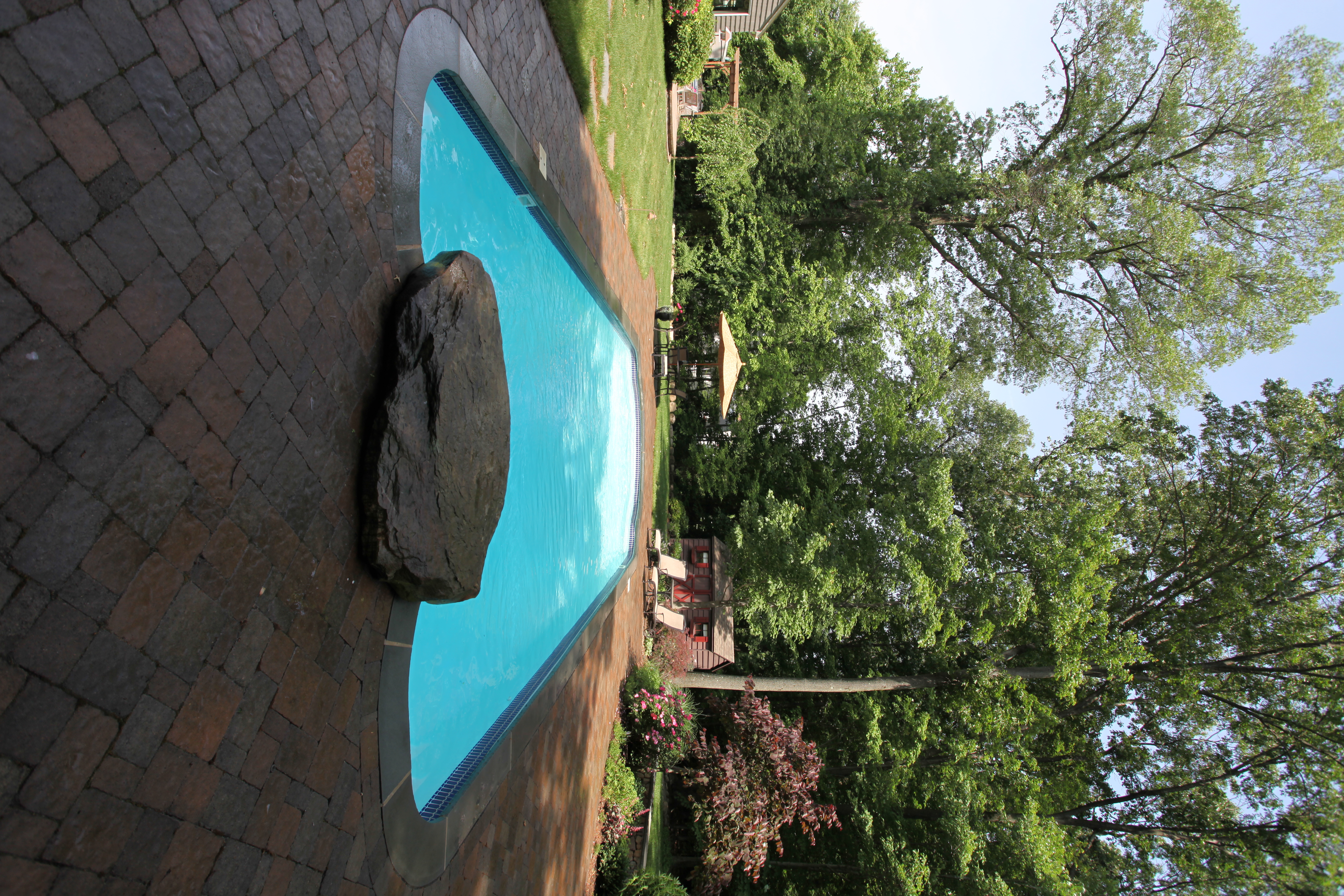 Enjoy the timeless elegance of a finished fiberglass in-ground pool with a sleek red-brick deck, perfect for sunny backyard relaxation.