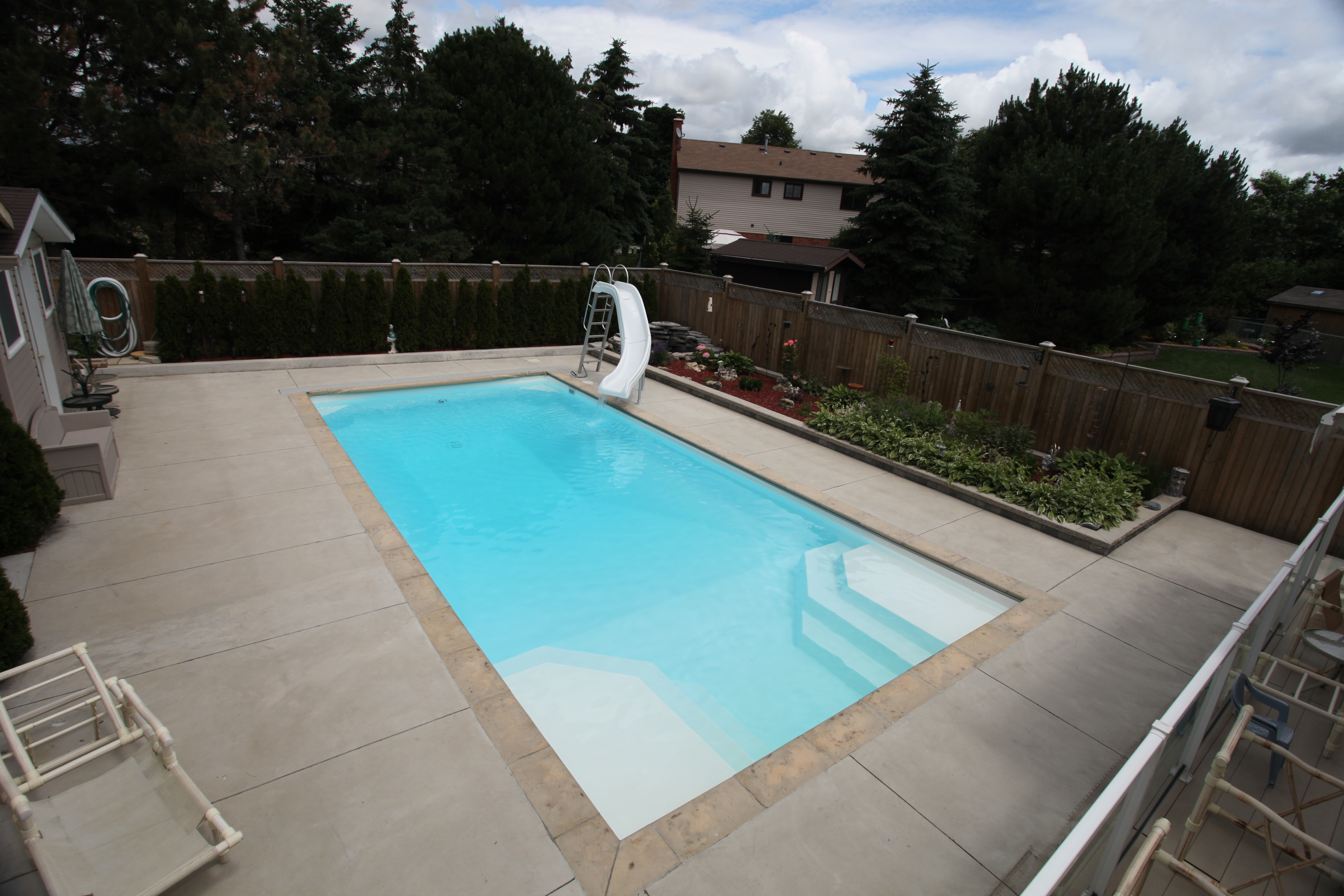 Enjoy a sunny, serene backyard with our new fiberglass pool, surrounded by lush greenery and a cozy outdoor kitchen – perfect for family fun and relaxation.
