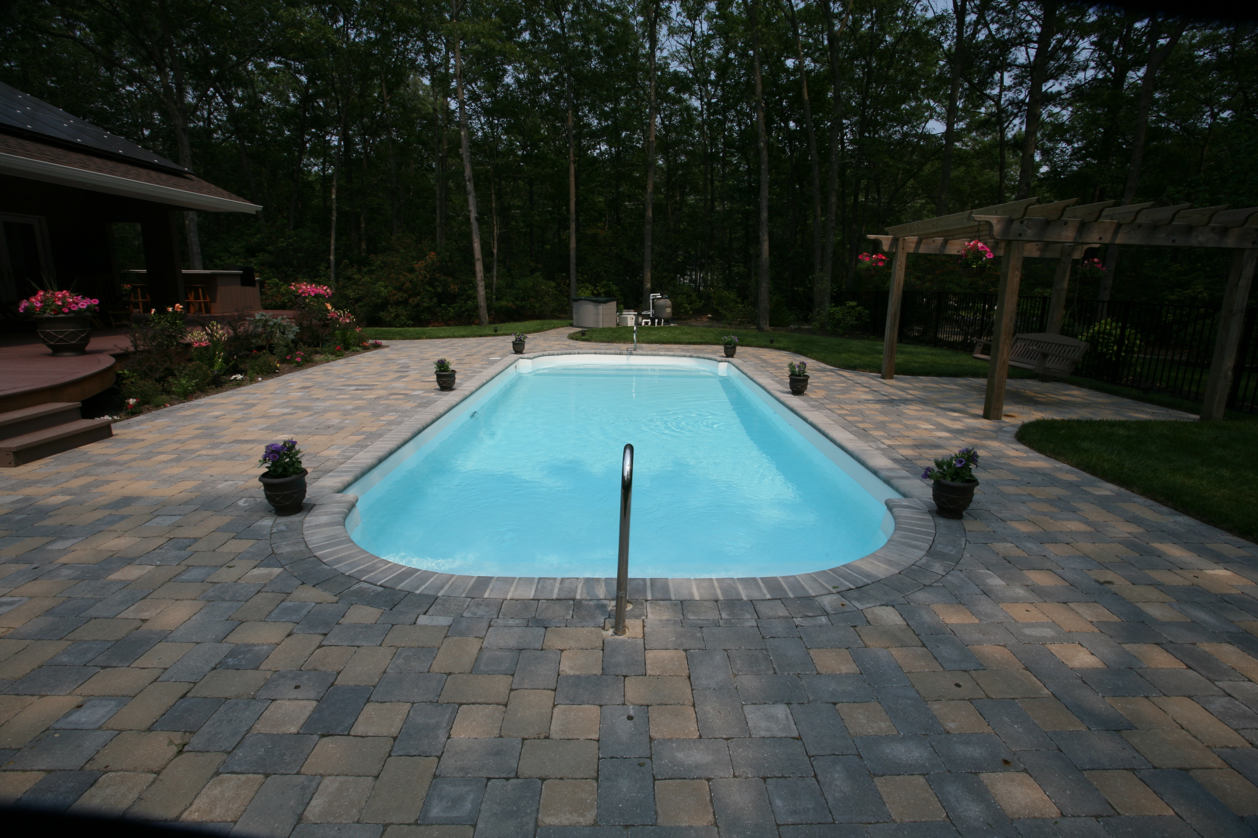 Relax and unwind in this beautifully maintained backyard featuring a gleaming fiberglass pool surrounded by lush greenery.