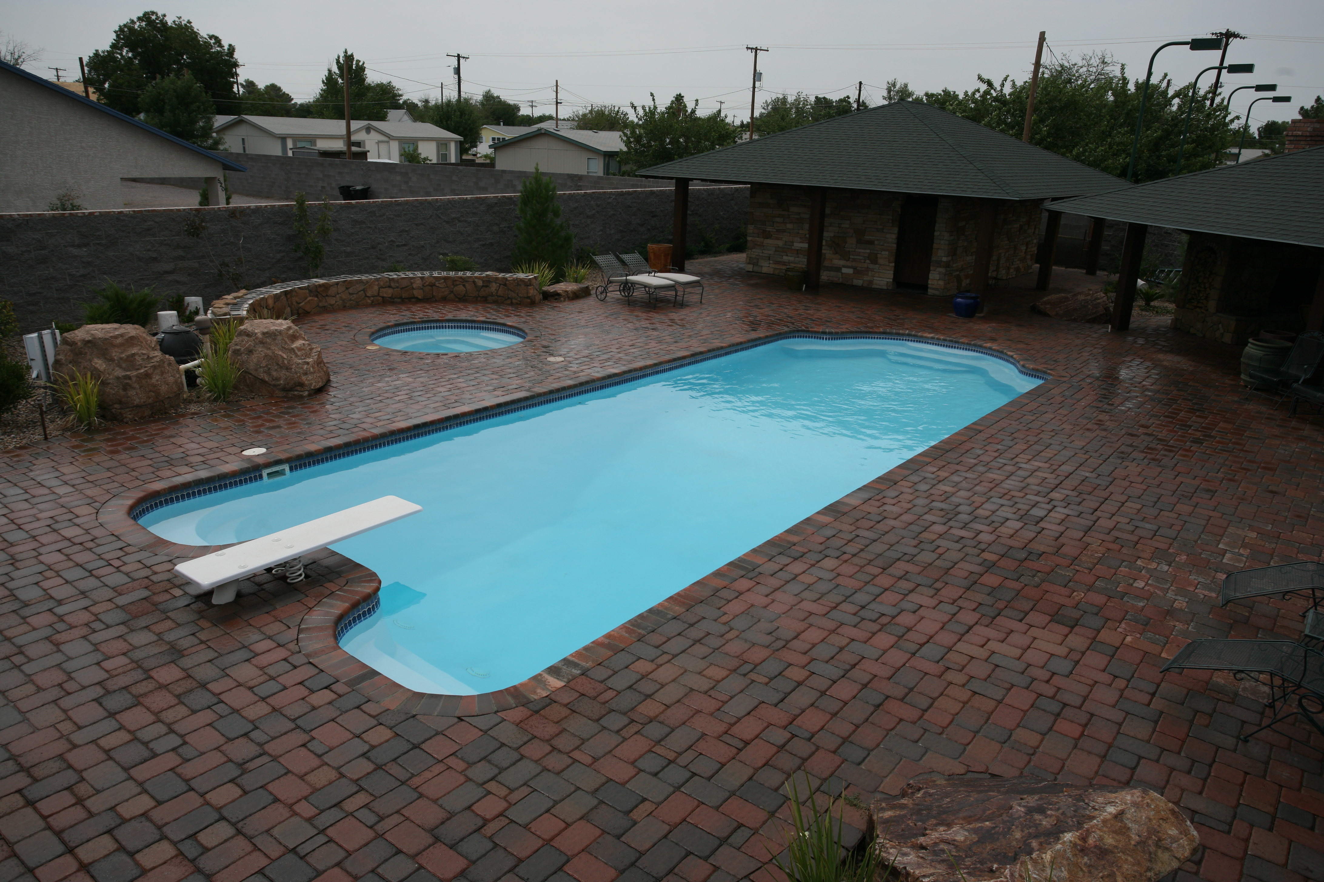 Experience a tranquil summer escape with our sleek fiberglass pool, nestled in a beautifully landscaped backyard complete with a brick paver patio, lush greenery, and comfortable lounge seating.