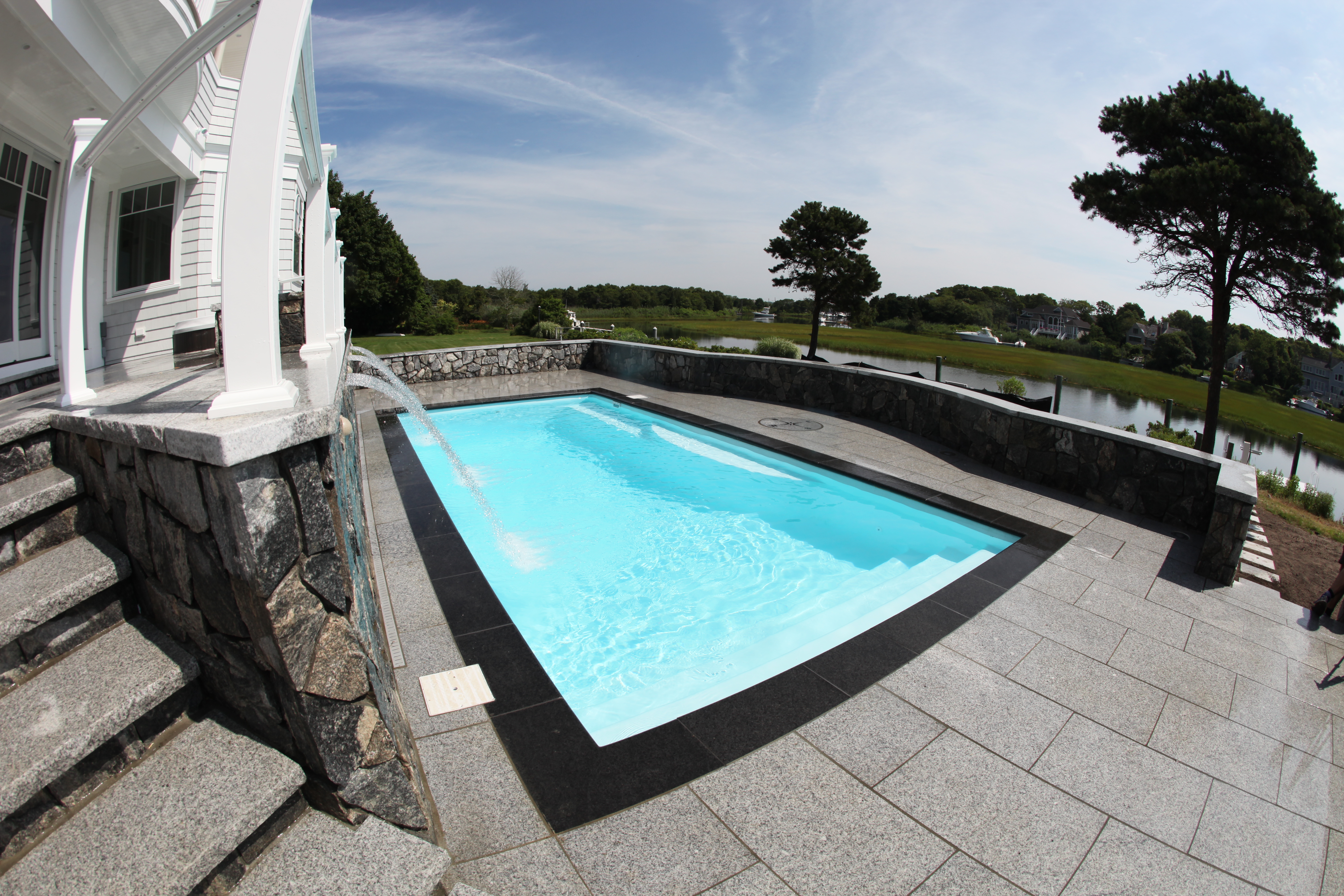 Enjoy the sparkling serenity of a new fiberglass pool, surrounded by a warm honey-colored deck, lush greenery, and a bubbling hot tub—perfect for summer relaxation.