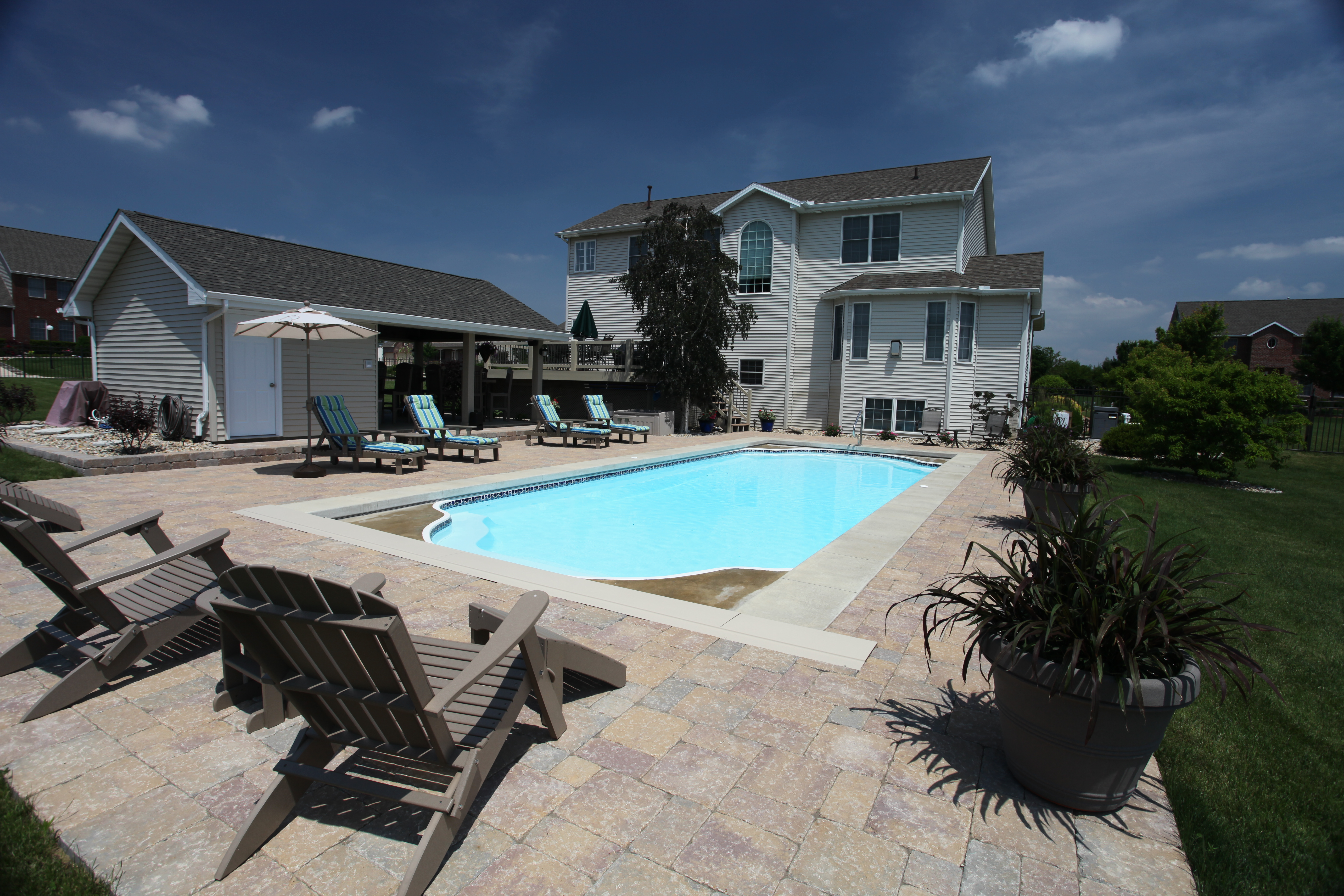 Enjoy a vibrant, ready for-use fiberglass pool in a lush backyard—bright blue water, lounge chairs, and a relaxed summer vibe.