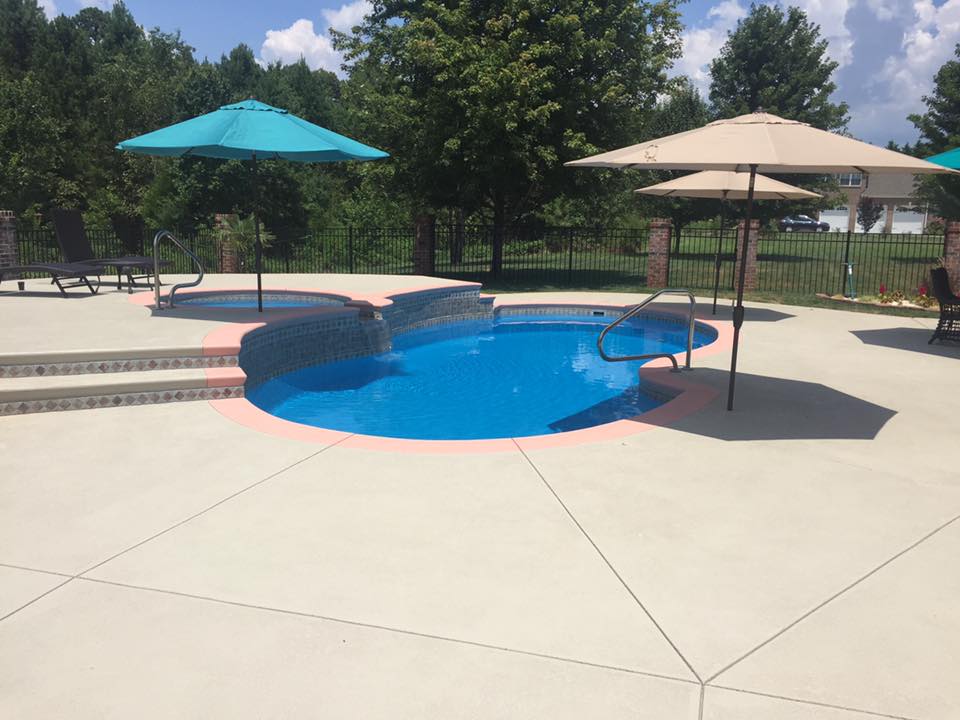 A pristine, fiberglass kidney-shaped pool basking in bright midday sun, set in a modern backyard oasis.