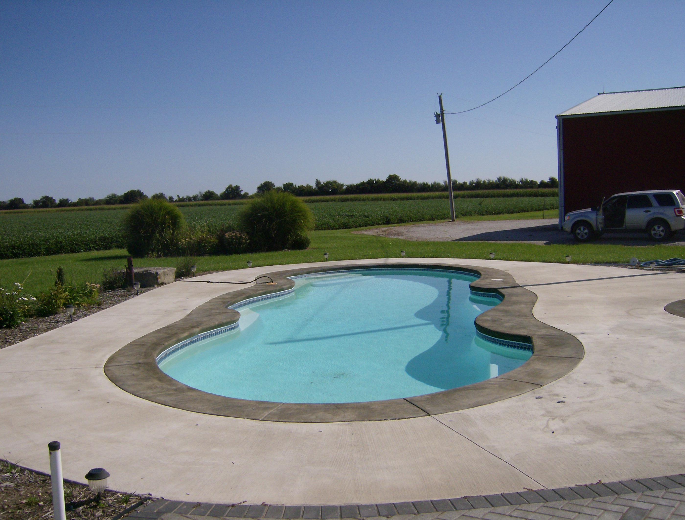 Experience tranquility with this serene fiberglass pool nestled in a rural backdrop, surrounded by lush greenery.