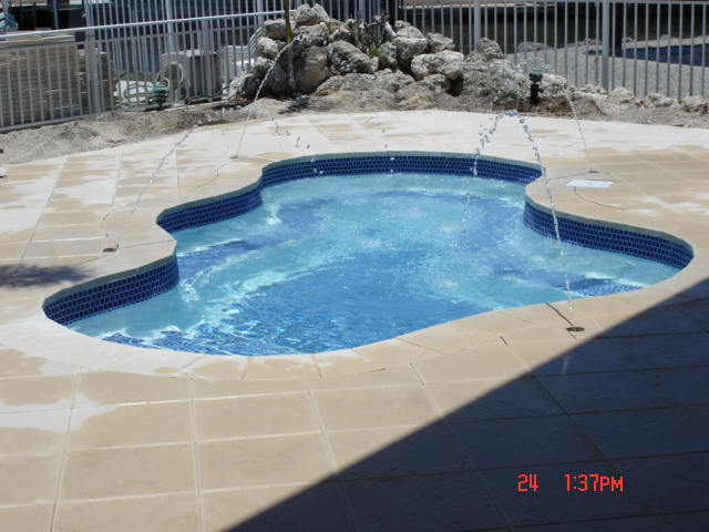 Sun-kissed fiberglass pool with deep-blue tile interior and sleek stone deck, perfect for relaxed summer leisure.