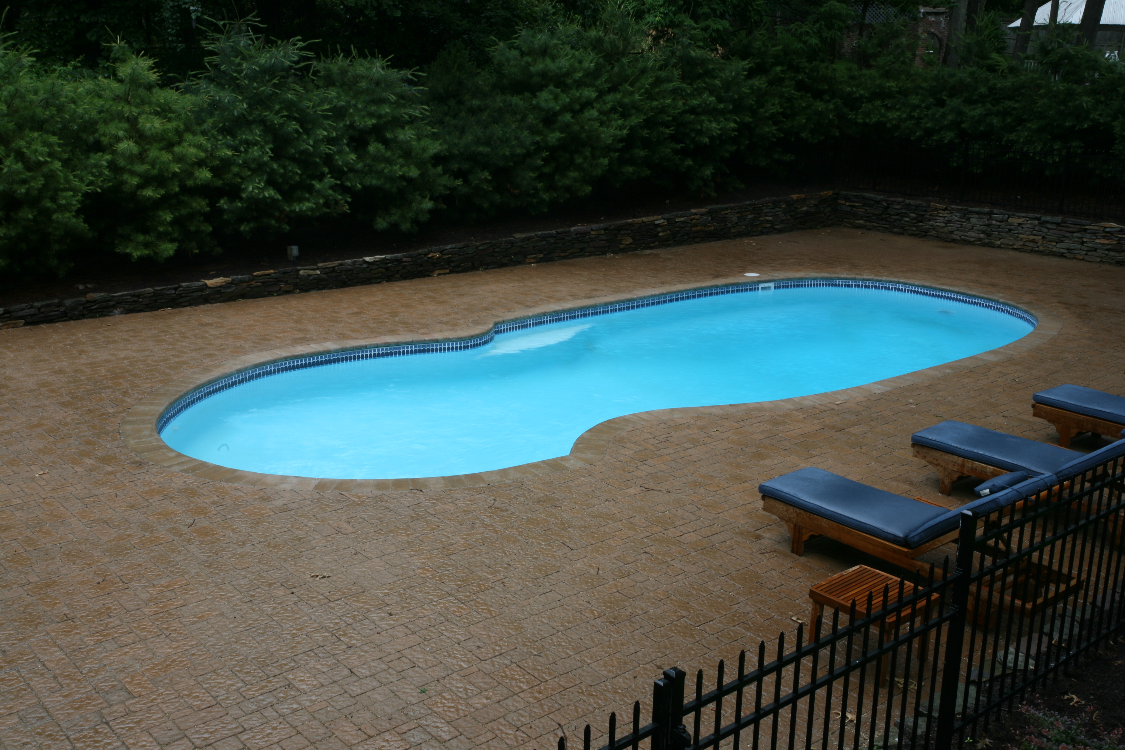 Discover the serene elegance of a fiberglass kidney-shaped pool, set in a private backyard oasis of calm blue water and natural greenery.
