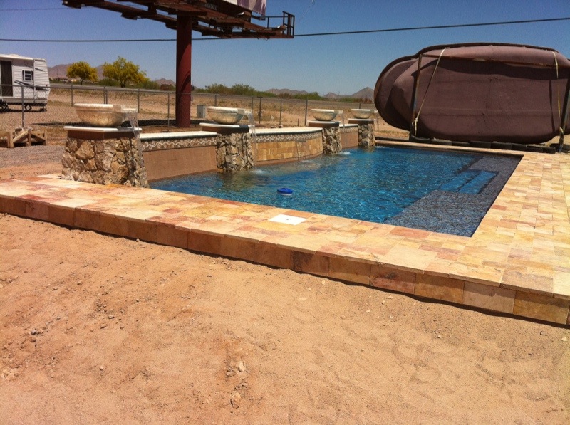 A sun-kissed desert backyard showcases a pristine fiberglass pool with vibrant blue water and a tiled deck, offering a refreshing oasis amid arid surroundings.