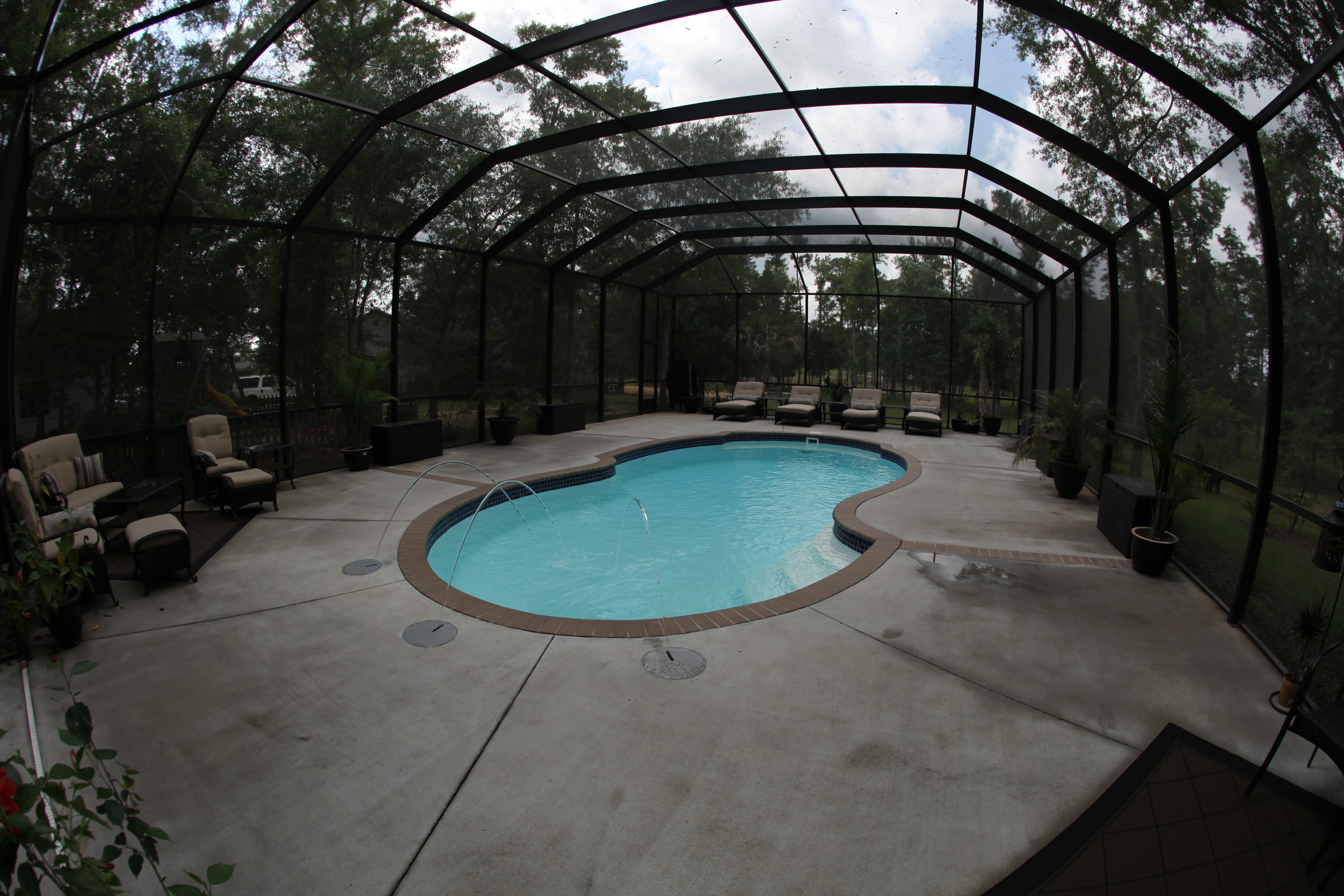 Escape to serenity with this kidney-shaped, light blue fiberglass pool, featuring three elegant fountain features and surrounded by lush greenery.