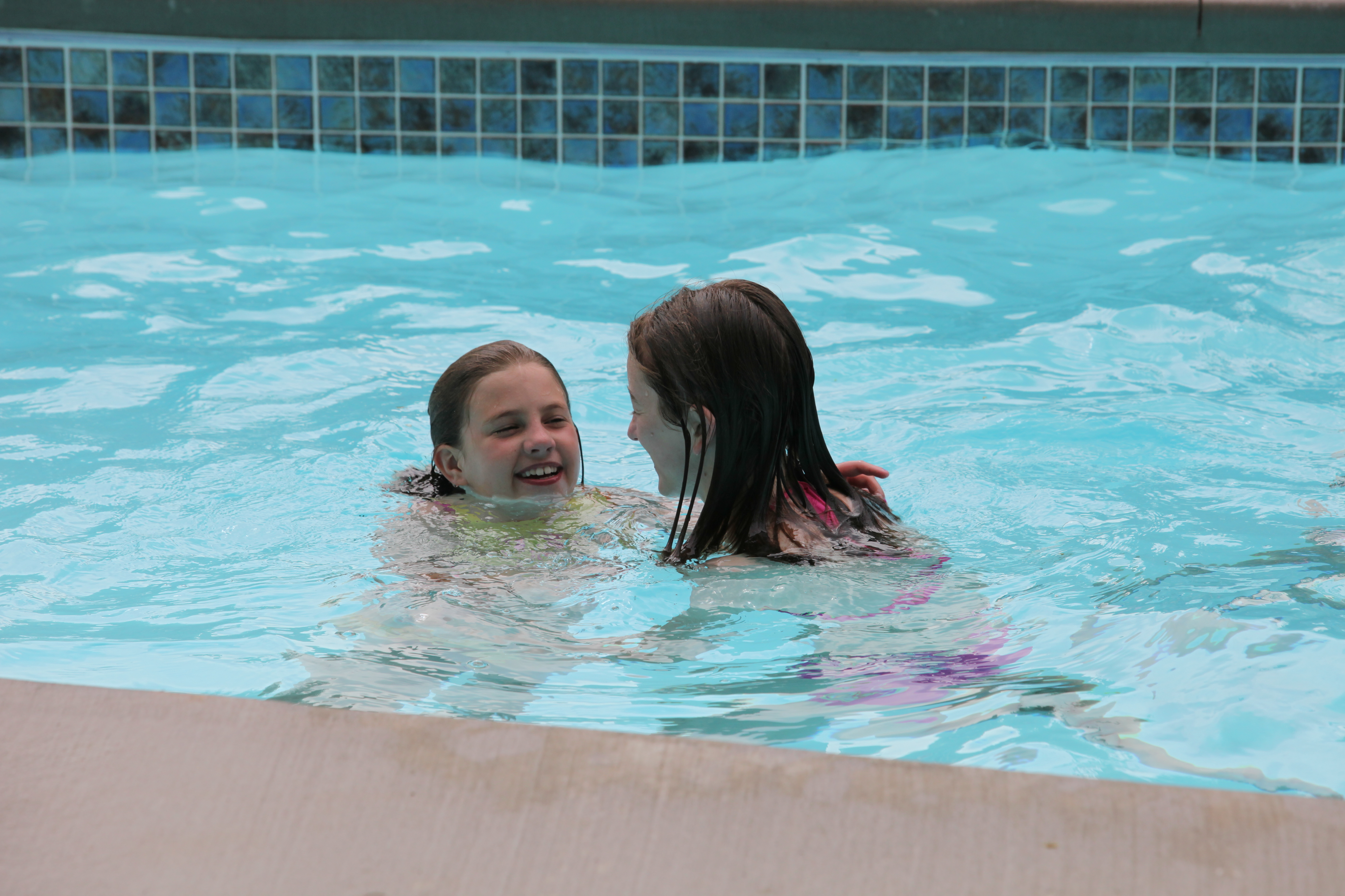 Two young girls engage in conversation while relaxing in a sparkling new fiberglass pool on a warm summer day.