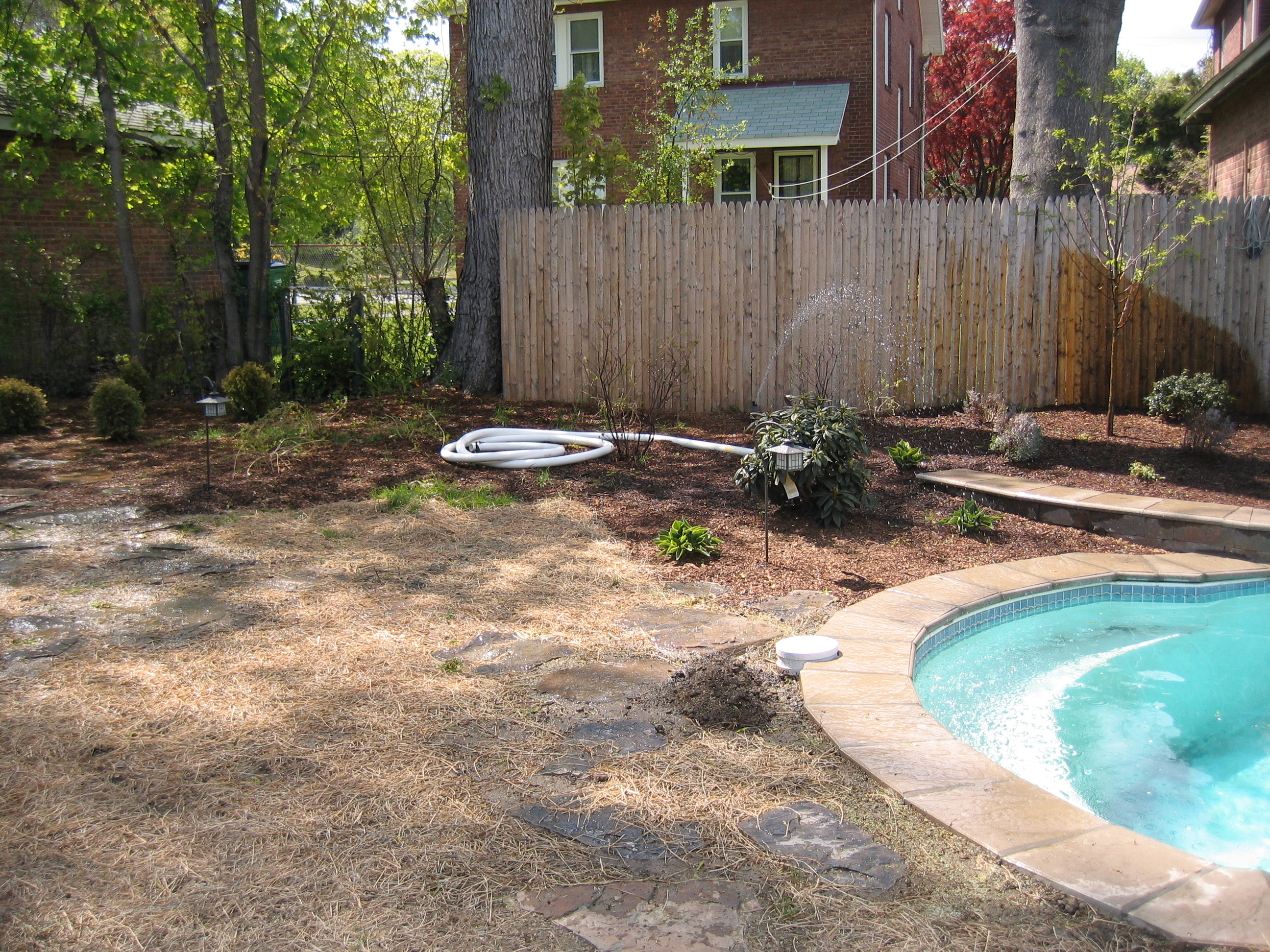 A sleek, fiberglass kidney-shaped pool creates a tranquil backyard oasis, framed by lush greenery and a natural stone patio.