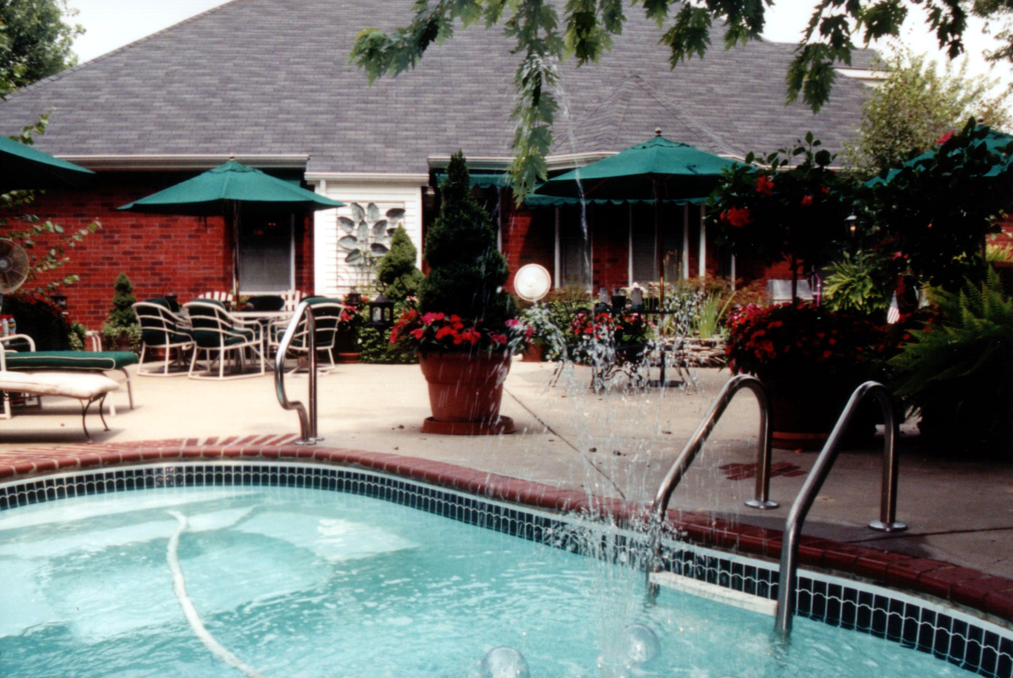 Experience relaxation with this fiberglass inground pool nestled amidst lush greenery and a calming fountain feature.