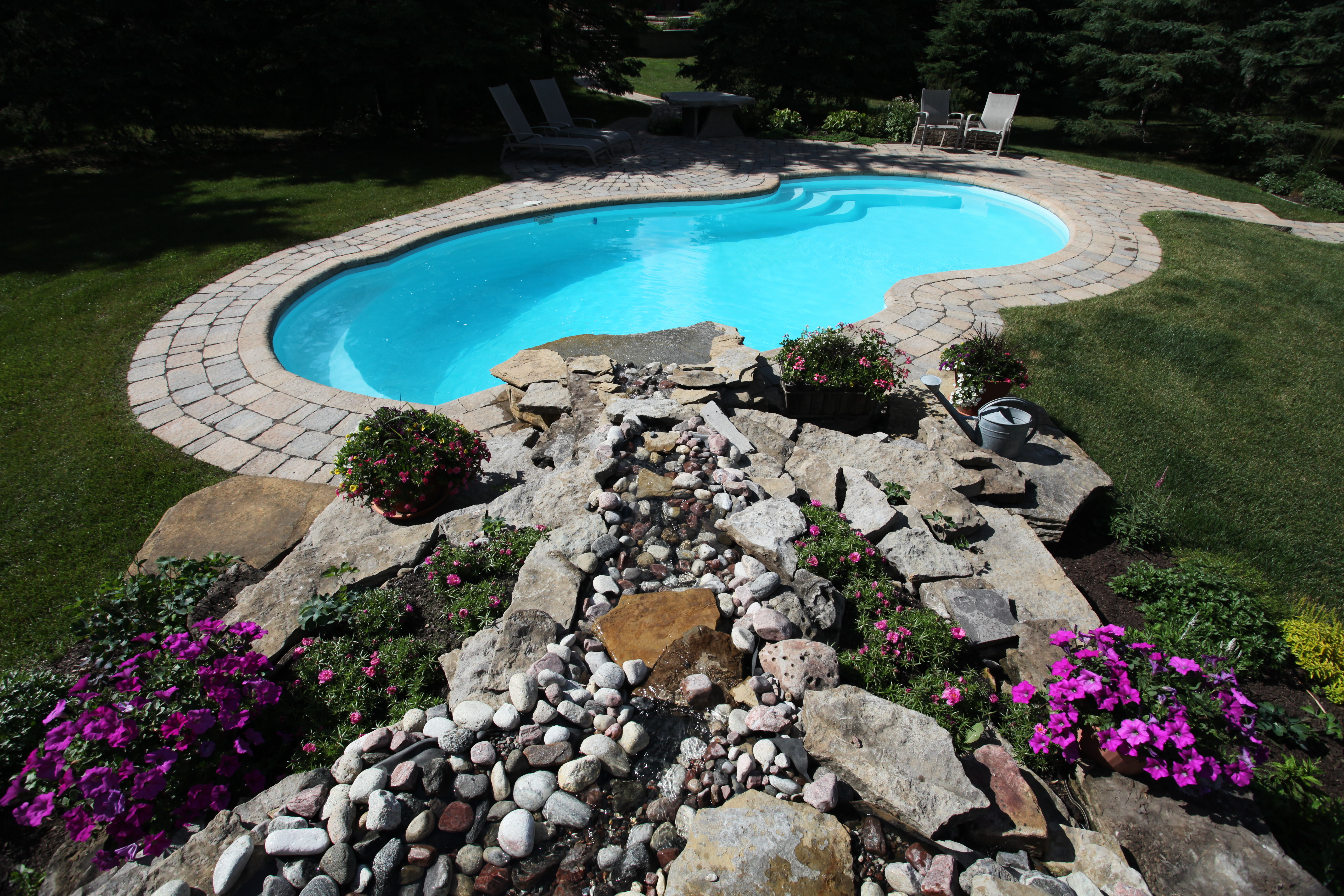 Relax in this serene backyard oasis featuring a stunning fiberglass kidney-shaped pool, surrounded by lush greenery and a well-maintained stone patio.