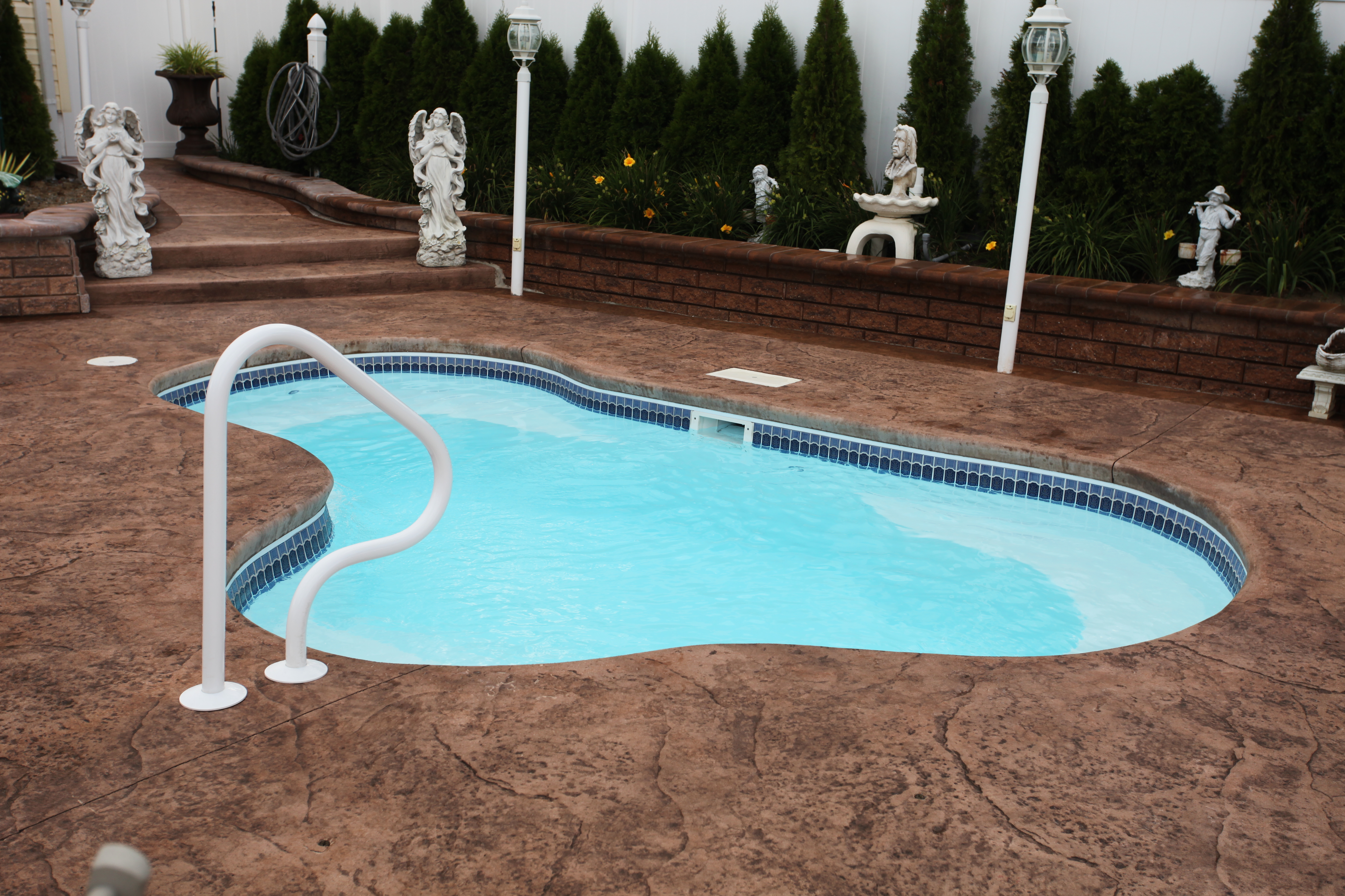 Experience backyard bliss with this sleek fiberglass kidney-shaped pool, nestled among lush landscaping and a stylish stamped-concrete patio.
