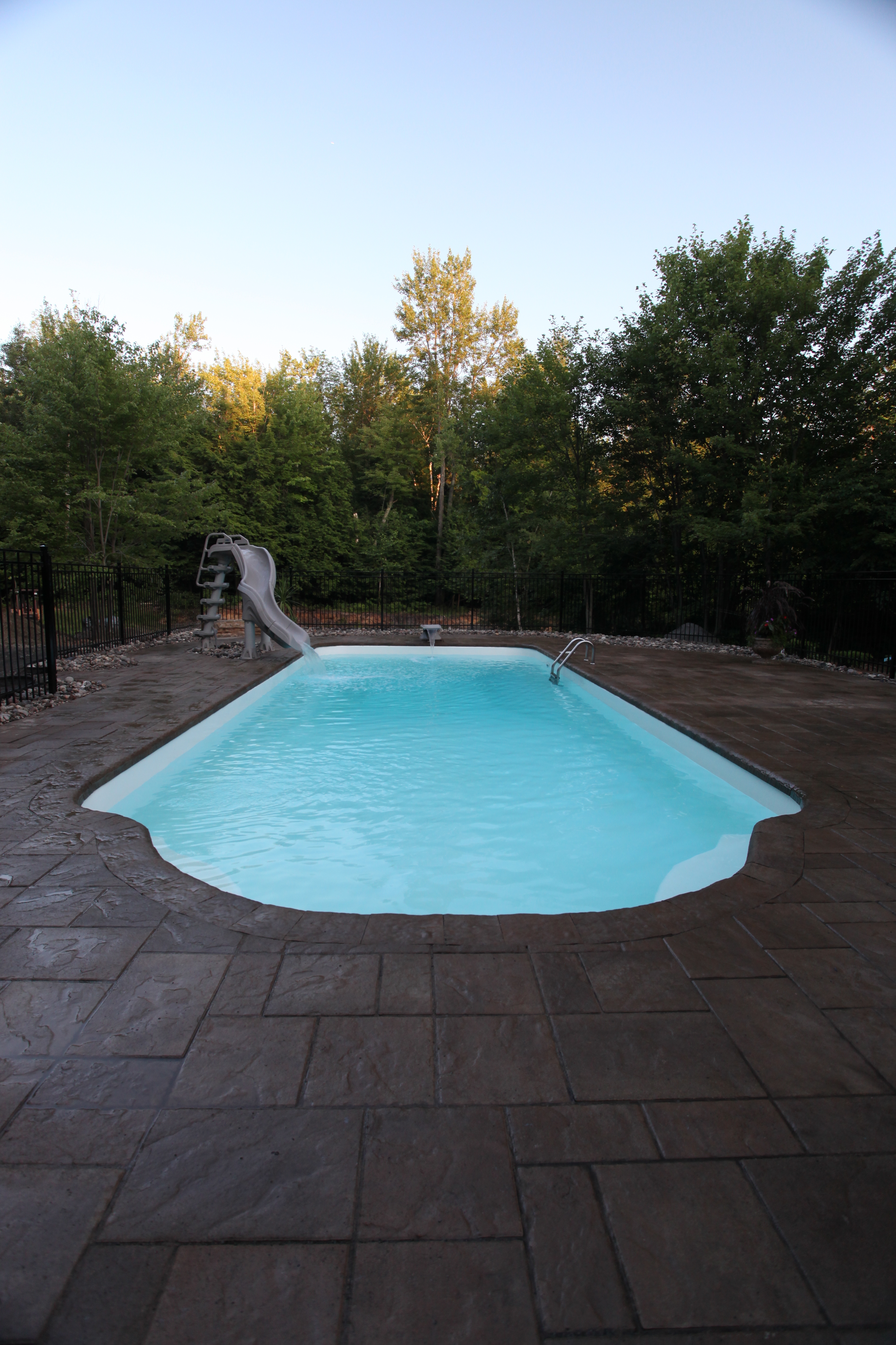 Immerse yourself in the serene beauty of this rectangular fiberglass pool, surrounded by a lush backyard oasis.