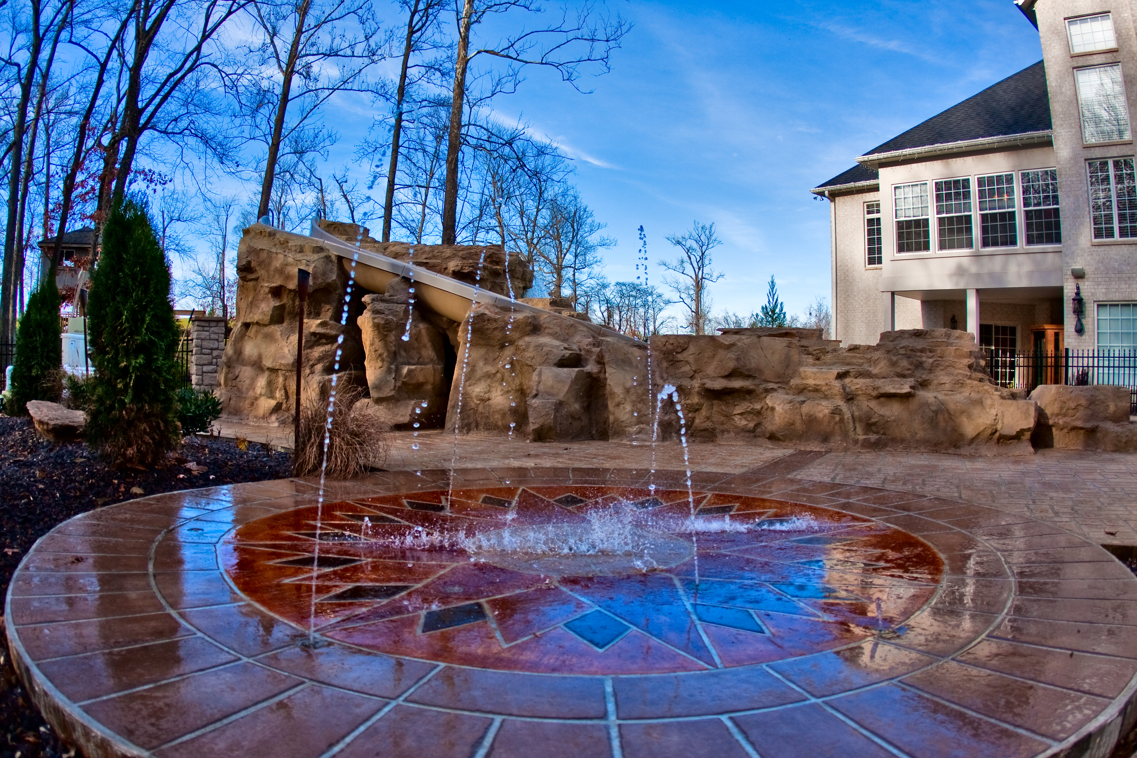 A serene backyard oasis in the desert southwest, featuring a unique water slide and rock formation, perfect for relaxation and entertainment. This modern outdoor space combines natural elements with luxurious amenities, creating a tranquil retreat for family and friends.