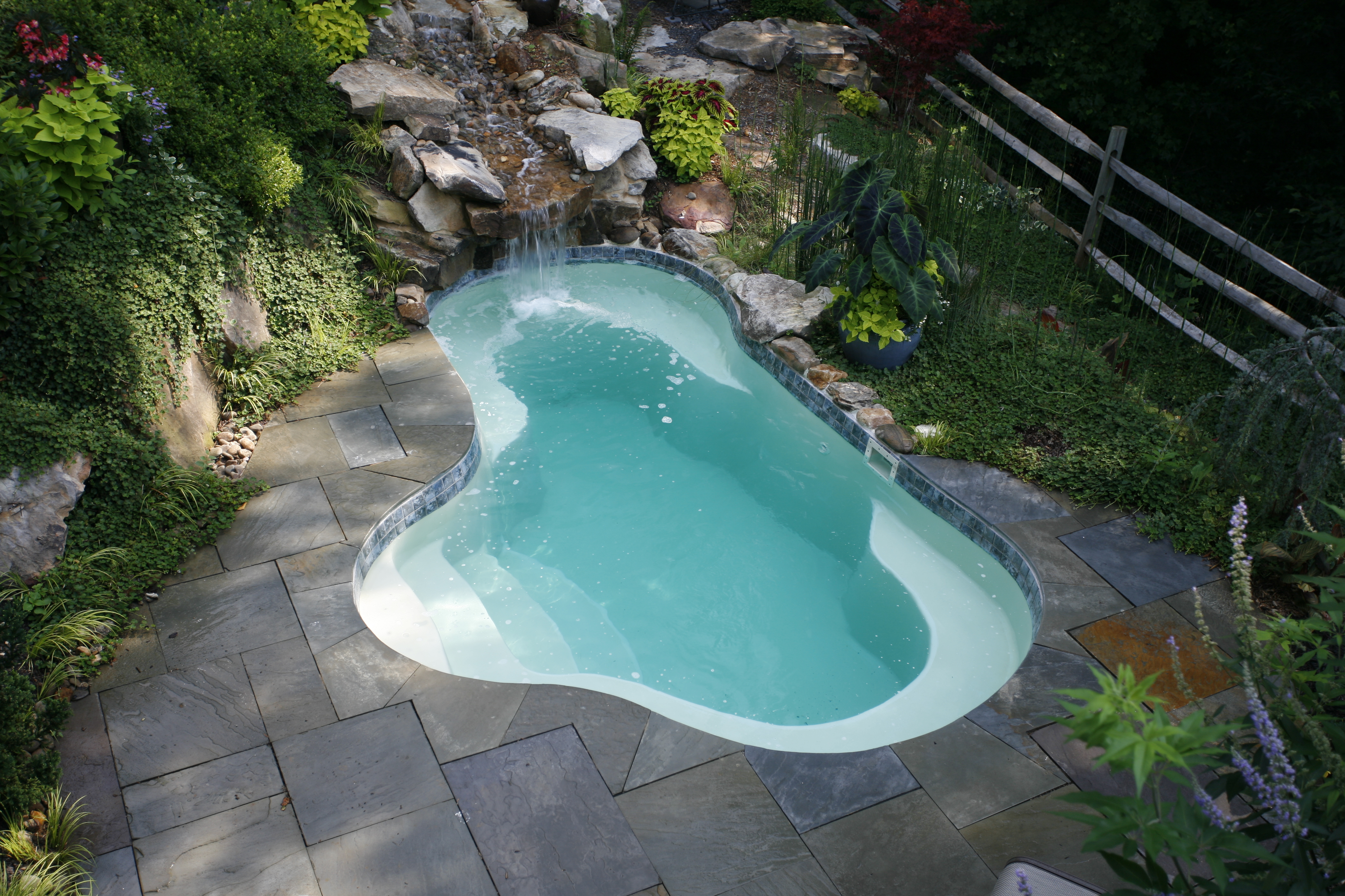 Experience relaxation at its finest with this uniquely shaped fiberglass kidney bean pool, surrounded by lush greenery and a soothing waterfall.