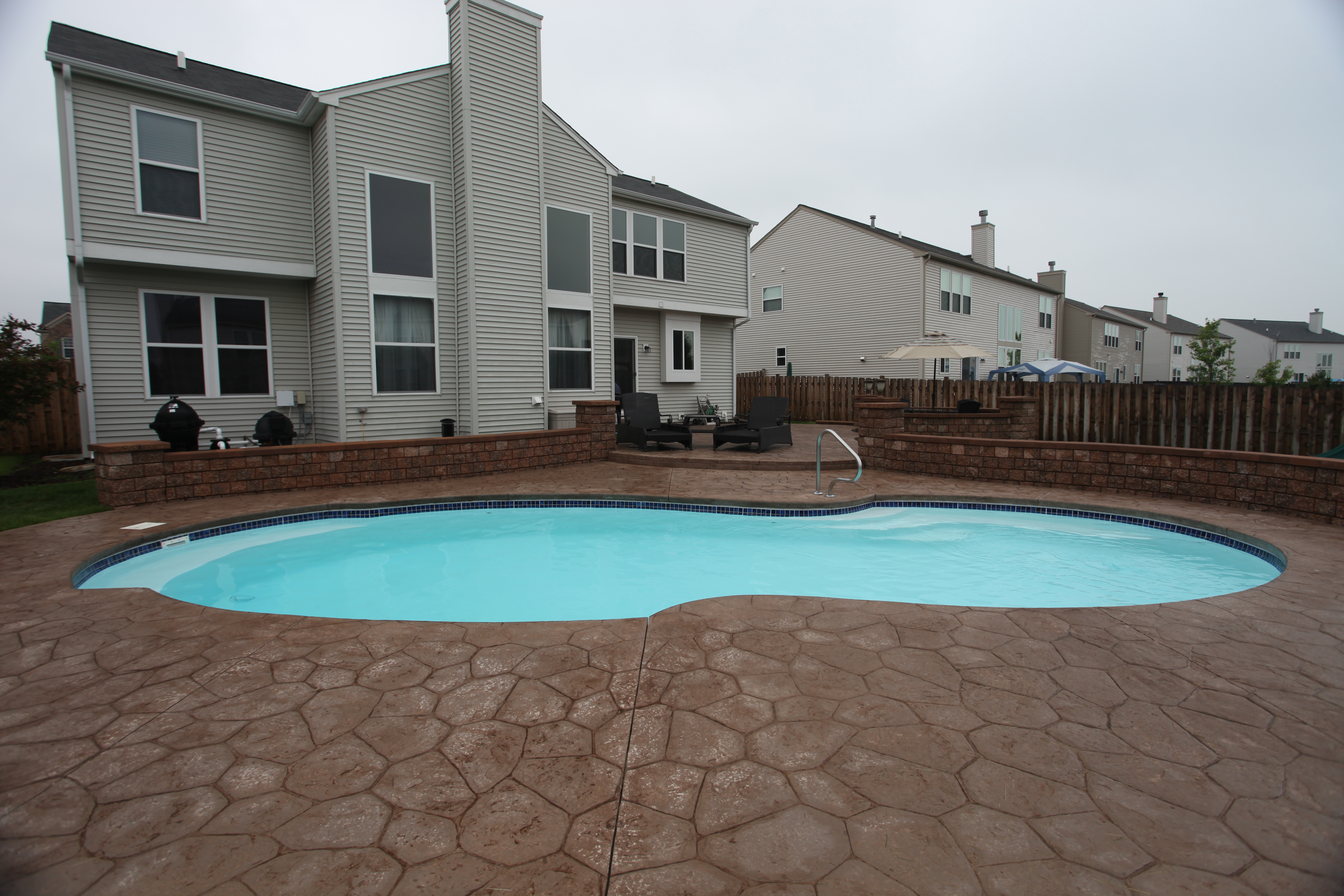 Relax by the kidney-shaped fiberglass pool, surrounded by a meticulously designed outdoor space with stone-patterned concrete and a modern aesthetic.
