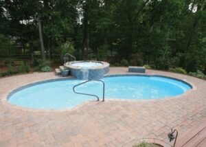 Finished oval fiberglass pool with turquoise water and brick patio in a sunny backyard.