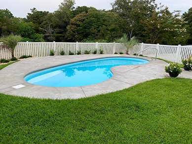 Fiberglass pool in a sunny backyard with a white picket fence.