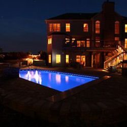Nighttime view of a rectangular fiberglass pool with dark blue water and warm house glow.